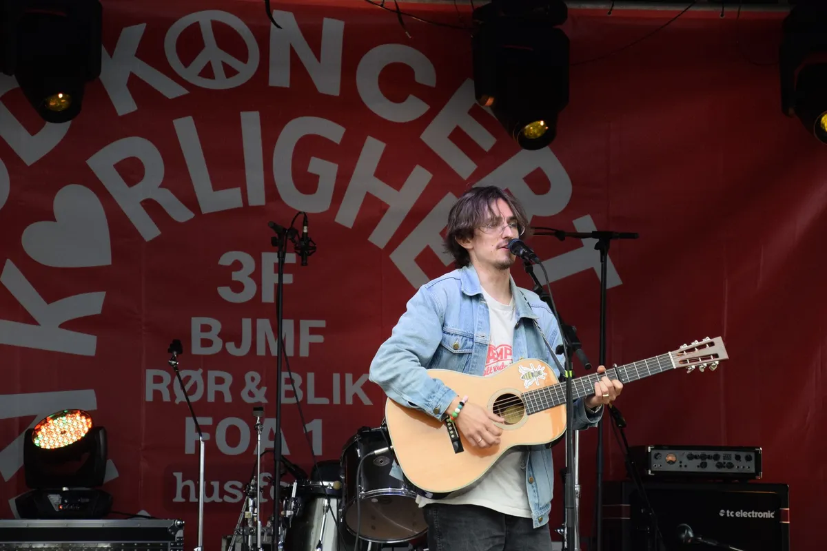 Jonas Mačys med guitar foran Hus Forbi og 3F på banneret