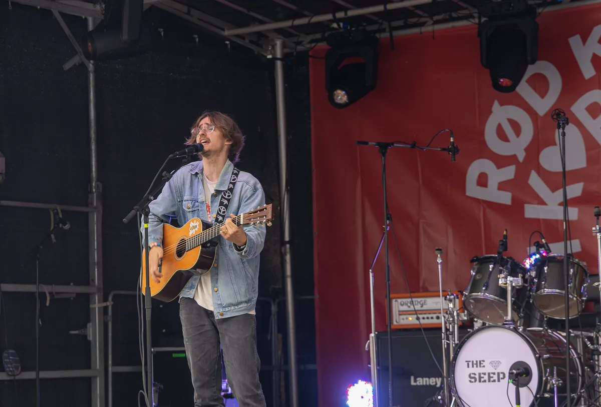 Jonas Mačys med akustisk guitar på scenen ved siden af trommesættet