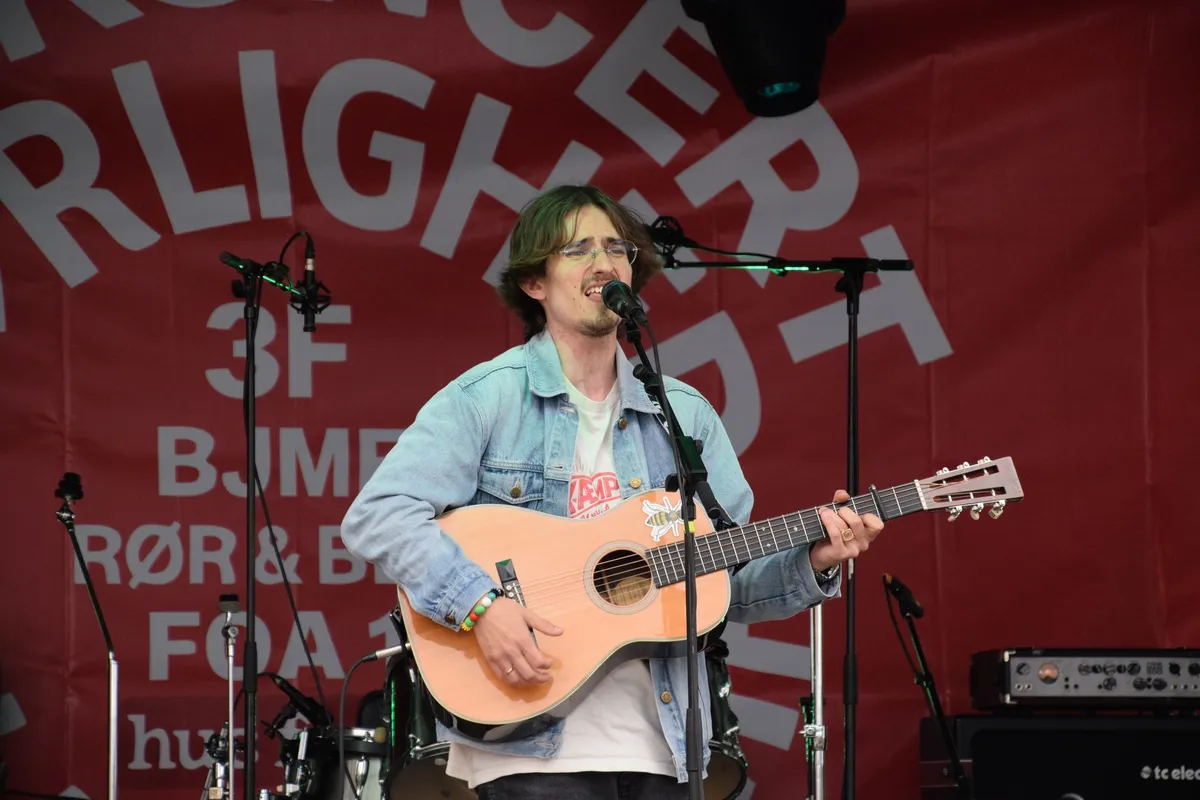 Jonas Mačys med guitar foran Rød Koncert-banneret