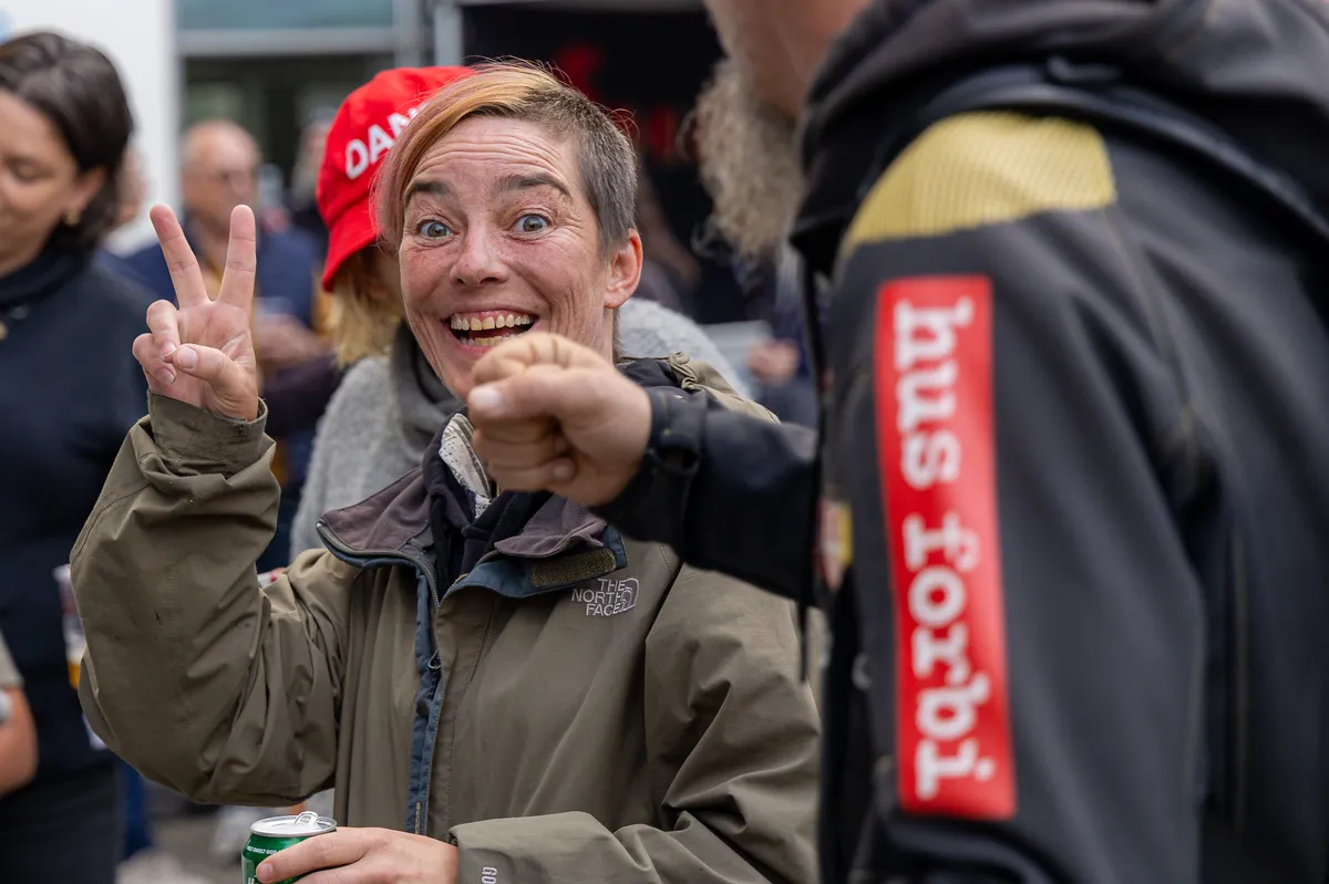 Glad gæst viser fredstegn med et Hus Forbi-mærke på ærmet i forgrunden