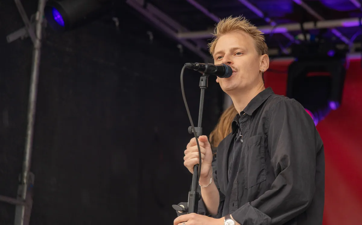 The Deadly Sons sanger synger i mikrofonen med rød baggrund